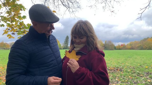 middle-aged woman and man tenderly hugging in autumn park among yellow and orange trees, leaf fall, heterosexual relationship concept, close-up