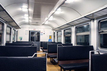 Interior of an empty train carriage with metal shelves and leather seats.