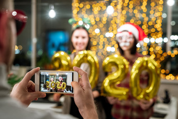 Hands of man holding smartphone with two young happy businesswomen on screen
