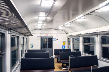 Interior of an empty train carriage with metal shelves and leather seats.