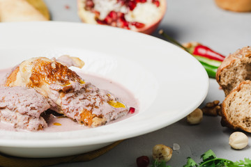 Close up of grilled chicken breast under pomegranate and walnut sauce on white plate on light stone background