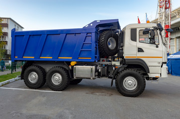 Fototapeta na wymiar Dump truck parked in the city. White cab, blue body. Side view.