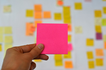 A hand is holding a pink blank sticker and there is a Kanban board of agile methodology on the...