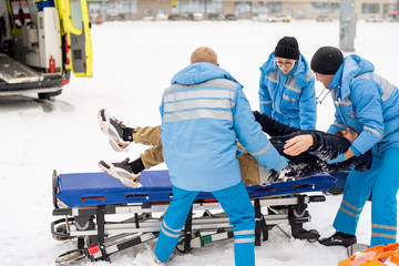 Brigade of paramedics in winter uniform putting unconscious man on stretcher