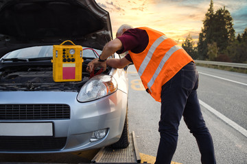 Road assistant worker in towing service trying to start car engine with jump starter and energy...
