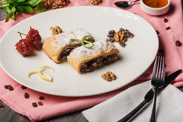 Homemade apple strudel on white plate, served with walnuts and cherry marinade. on the pink napkin