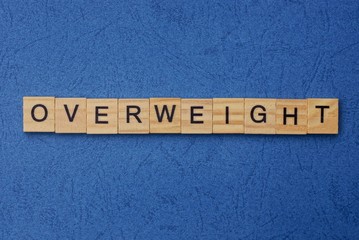 word overweight made from brown wooden letters lies on a blue table
