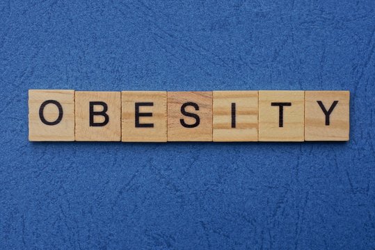 word obesity made from brown wooden letters lies on a blue table