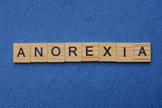 word anorexia made from brown wooden letters lies on a blue table