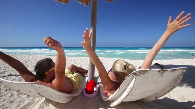Caribbean christmas celebration. Couple relaxing on beach. Looking to the sea and show something. Enjoying life. New Year on seashore. Travel destinations. Summer vacations