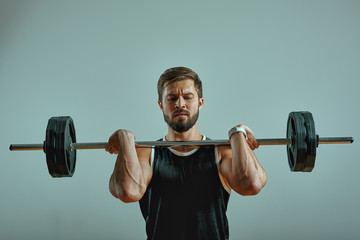 Fototapeta Portrait of super fit muscular young man working out in gym with barbell on gray background, copyspace. obraz