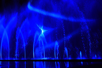 Colorful water fountains. Beautiful laser and fountain show. Large multi colored decorative dancing water jet led light fountain show at night. Dark background.