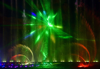 Fototapeta na wymiar Colorful water fountains. Beautiful laser and fountain show. Large multi colored decorative dancing water jet led light fountain show at night. Dark background.