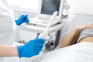 A gynecologist sets up an ultrasound machine to diagnose a patient who is lying on a couch. A transvaginal ultrasound scanner of the internal organs of the pelvis. Female health concept - obrazy, fototapety, plakaty