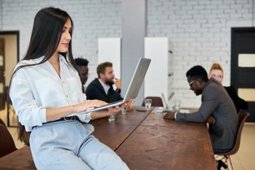 Side view on beautiful woman using laptop in her workplace, portrait of woman in white shirt holding laptop