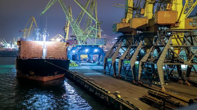 China. Cargo operation with bulk carrier vessel moored at pier. Big cargo terminal at seaport. Cereals bulk transshipment from road transport to vessel at night. Agricultural products transport.
