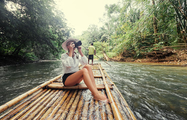 Traveling by Thailand. Pretty young woman taking photo sailing jungle river on traditional bamboo...