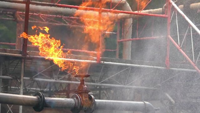 HD Slow motion of firefighter on safety rescue duty using water extinguisher spraying water from a hose extinguishing to control crackle fire flames from gas pipeline leaking. Fireman fighting a fire.
