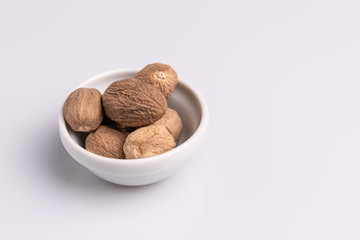 Nutmeg spice in a ceramic bowl isolated on white background, soft light, studio shot, copy space