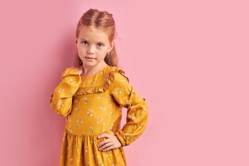 Little cute and beautiful girl in yellow dress look at camera posing. Pink isolated background