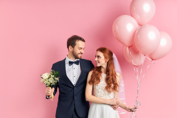 Handsome man in tuxedo and redhaired woman in wedding dress look at each other with love. Holding...