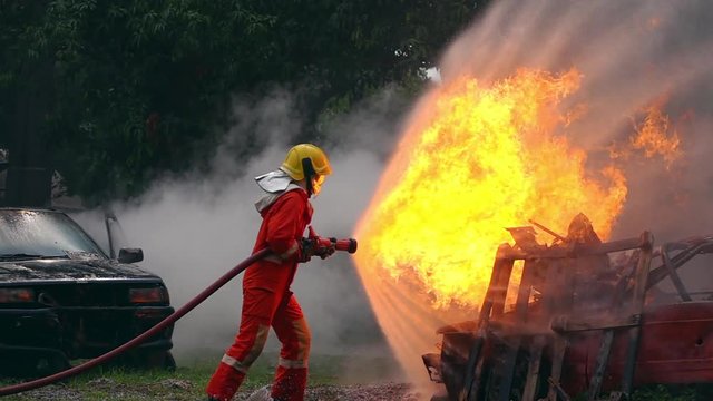 HD Slow motion wide shot of firefighter in fire suit on safety rescue duty using water extinguisher from a hose extinguishing crackle fire flames inside burning premises. Fireman fighting a fire.