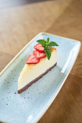 Piece of delicious cheesecake with strawberry and mint leaves on white plate.