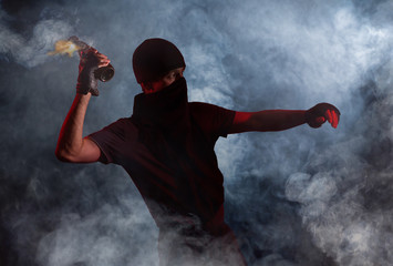 A protesting man in puffs of smoke throws a burning bottle. Studio photography