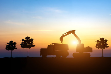 Silhouette of excavator and truck at construction site on sunset. Heavy machine equipment for...
