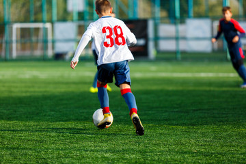 Boys in white and blue sportswear plays  football on field, dribbles ball. Young soccer players with ball on green grass. Training, football, active lifestyle for kids concept 