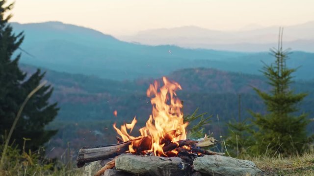 Bright campfire flames burning on top of mountain at evening time. Picturesque mount landscape and forest nature. Camping. Peace and inspiration.