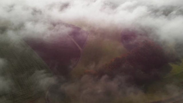A morning with fog in a rural area of Luxembour, a tilt up revealing a windturbine. Aerial shot.