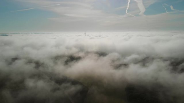 Aerial shot above the morning fog in Luxembourg showing windturbines.
