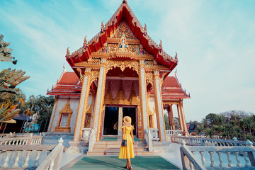 Obraz premium Travel by Asia . Young woman in hat and yellow dress walking near the Chalong buddhist temple on Phuket Island in Thailand.