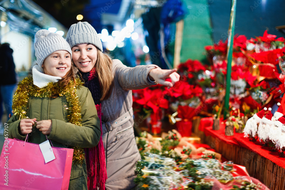 Wall mural Young girl and her mother are buying Christmas ornamentals in the market outdoor.