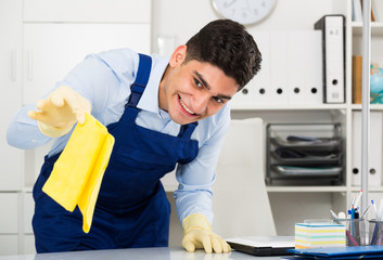 Male cleaner 25-30 years old is cleaning dust from the desk