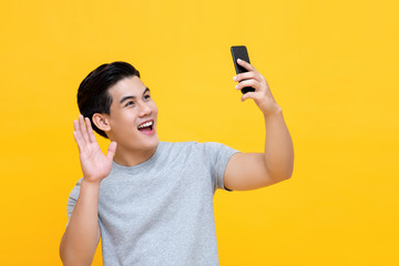 Smiling Asian man waving hand while making video call on smartphone