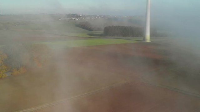 Revealing aerial shot of a rural area in Luxembourg showing a windturbine, during a morning with fog.