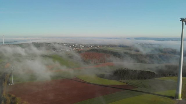 A morning with fog in a rural area of Luxembourg with a view of a windturbine and a road. Aerial shot.