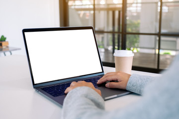 Fototapeta premium Mockup image of a woman using and typing on laptop with blank white desktop screen with coffee cup on the table
