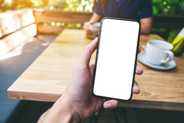 Mockup image of a man holding black mobile phone with blank white screen with woman drinking coffee in cafe