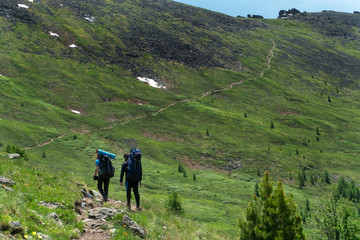 Hiking with backpacks on a beautiful rocky trail on a warm sunny day. The concept of family travel and adventure.