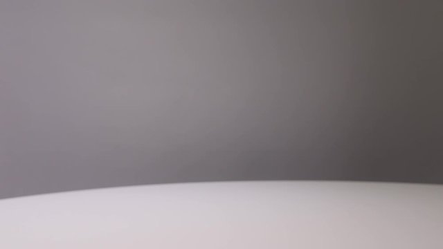 Video showing cocktail glass and woman's left appearing and picking up cocktail glass with red colored cocktail or mocktail on white table gray background. Drink concept. Selective focus. Copy space.