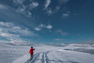A middle age woman pointing to snowy roads in bright sportive clothes; winter natural background with snow fields, trees in frost, frozen lake, mountains; active healthy lifestyle; trekking path; Ural