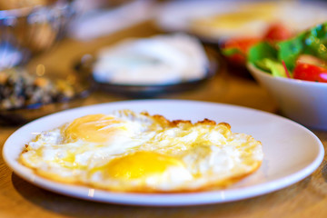 Fried eggs in a white plate with salad for breakfast on a wood table. Soft selective focus.