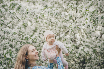 beautiful woman holding child. March 8: women among flowers. Baby in fly. the concept of congratulations, women's holidays, natural make up