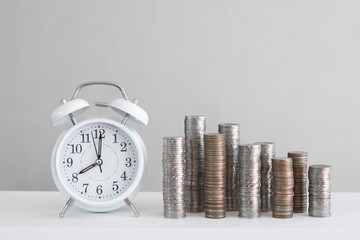 Alarm clock and coin piles arrange into growth chart on white background, finance and business concept