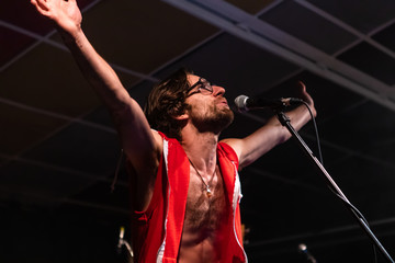 A low angle view of a male musician is viewed from behind as he sings deeply and Reacts with his...