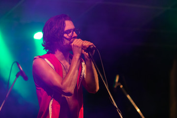 A male musician is viewed from the side as he sings and interacts with the audience under the spotlights with a dark background