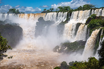 Panoramic view to cascading water falls, brown river and blue sky, Iguazu Falls, Argentina